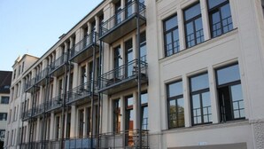 Ein mehrgeschossiges Gebäude mit einer symmetrischen Fassade, das Balkone auf jeder Etage, große Fenster und einen klaren, modernen Baustil aufweist.