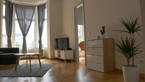 A modern living room with a sofa, a TV, a small table, a cabinet, and a potted plant. - Apartment-Superior-Ensuite (Leipzig)