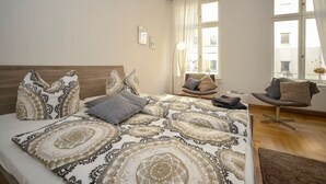 A bedroom with a large bed, a chair, and a desk. - Apartment-Superior-Ensuite (Leipzig)