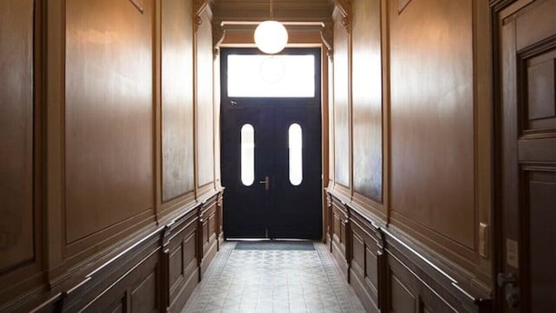 A hallway with a patterned floor, a double door at the end, and a round light fixture above. - Apartment-Superior-Ensuite (Leipzig)