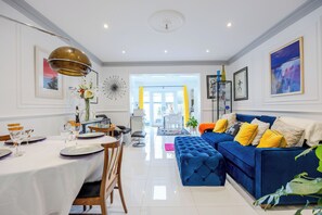 A modern living room with a blue sofa, dining table set, and a bright, well-lit space with a view to the outside. - Wavertree Hotel (London)
