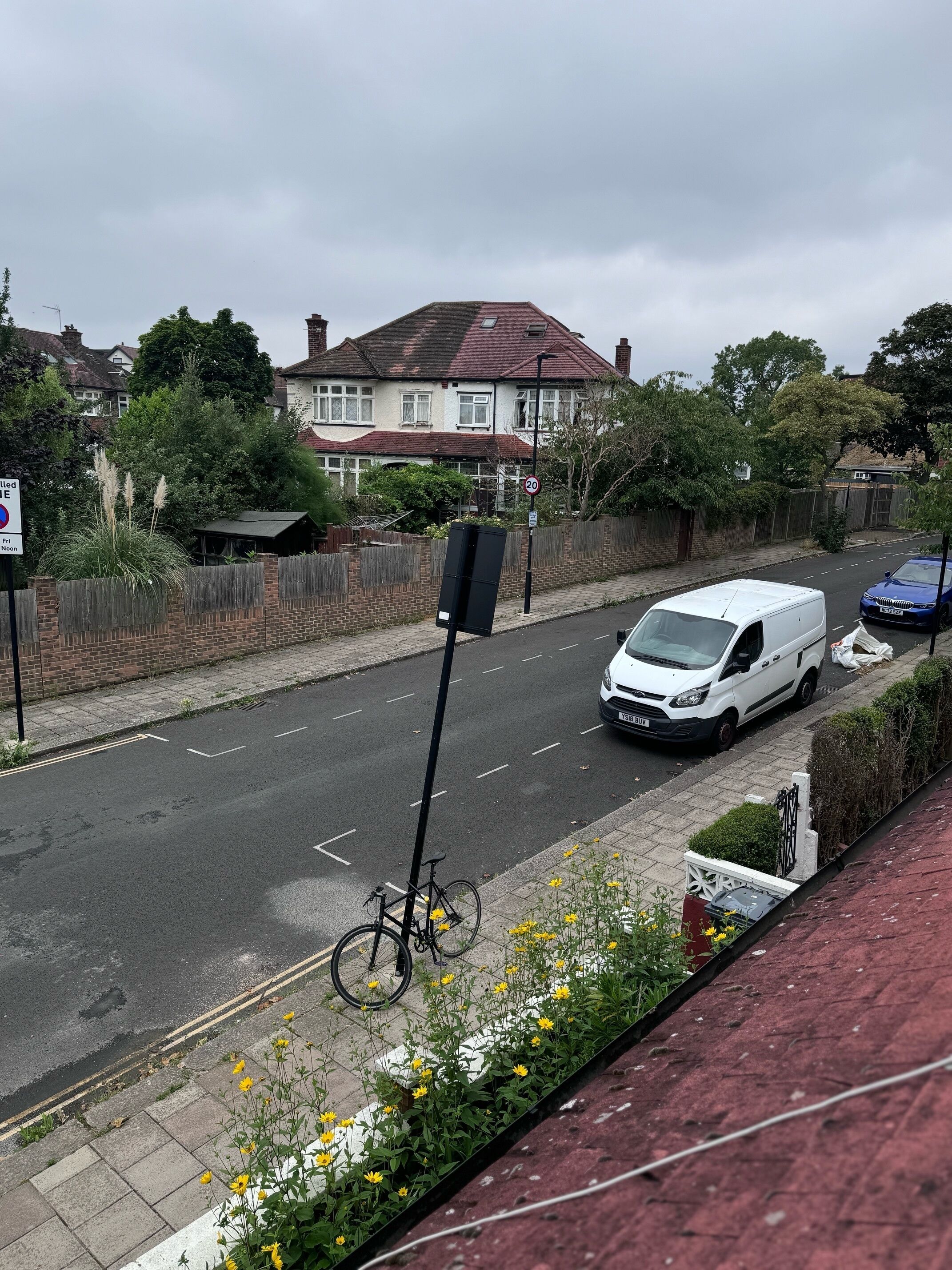 Une vue de rue avec un fourgon blanc garé sur le bord, un vélo appuyé contre un poteau et un bâtiment en briques rouges en arrière-plan.