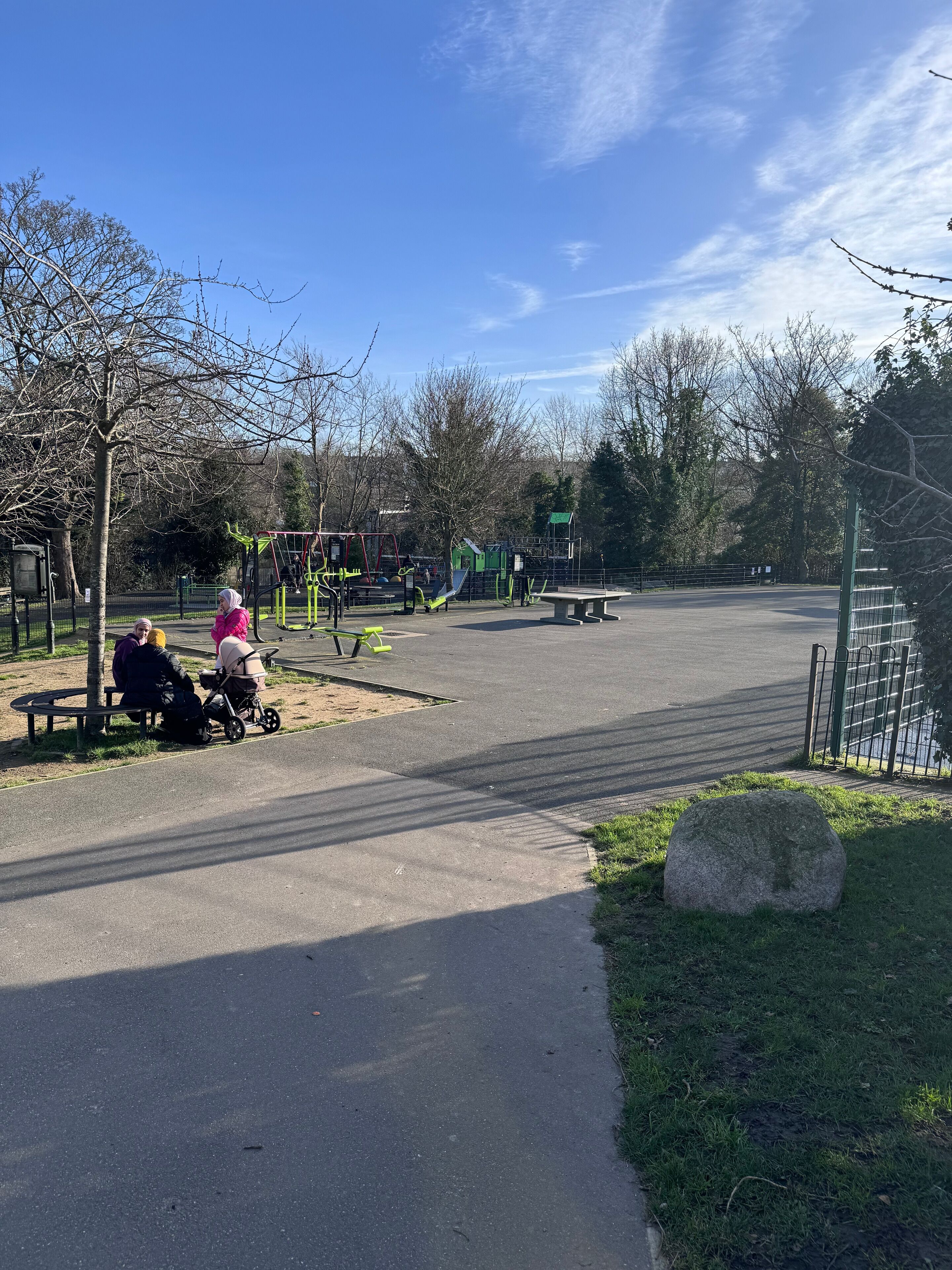 A park with exercise equipment, benches, and a paved path.