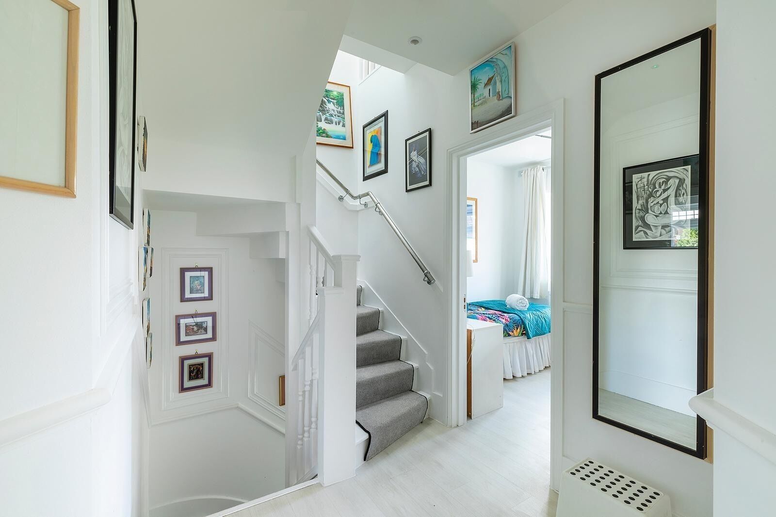 A staircase leading to a bedroom with a bed, a window with curtains, and framed artwork on the walls.