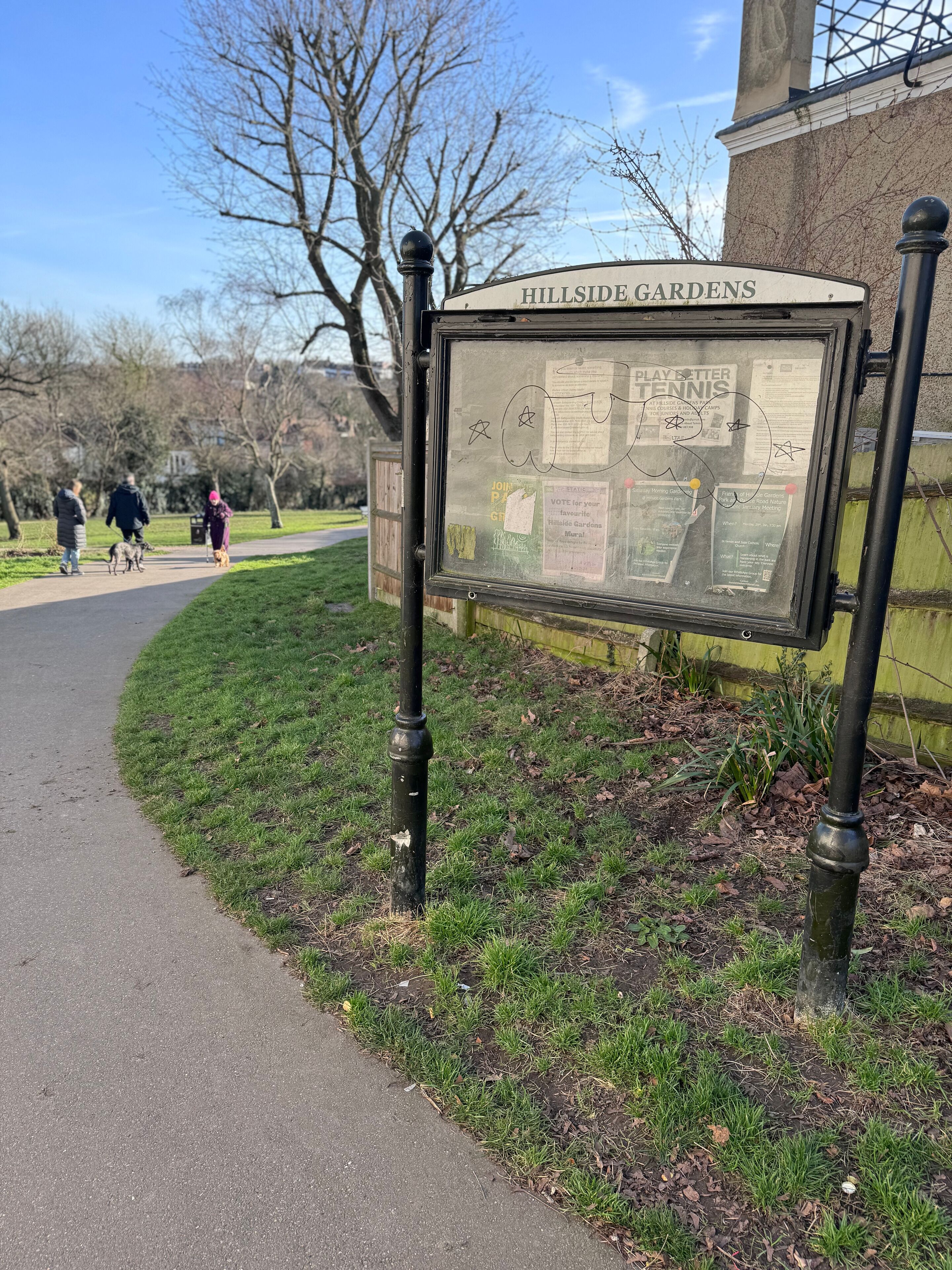 A sign for Hillside Gardens with a path and people walking nearby.