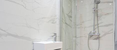 A modern bathroom with a glass-enclosed shower, a white sink, and a red bath mat.