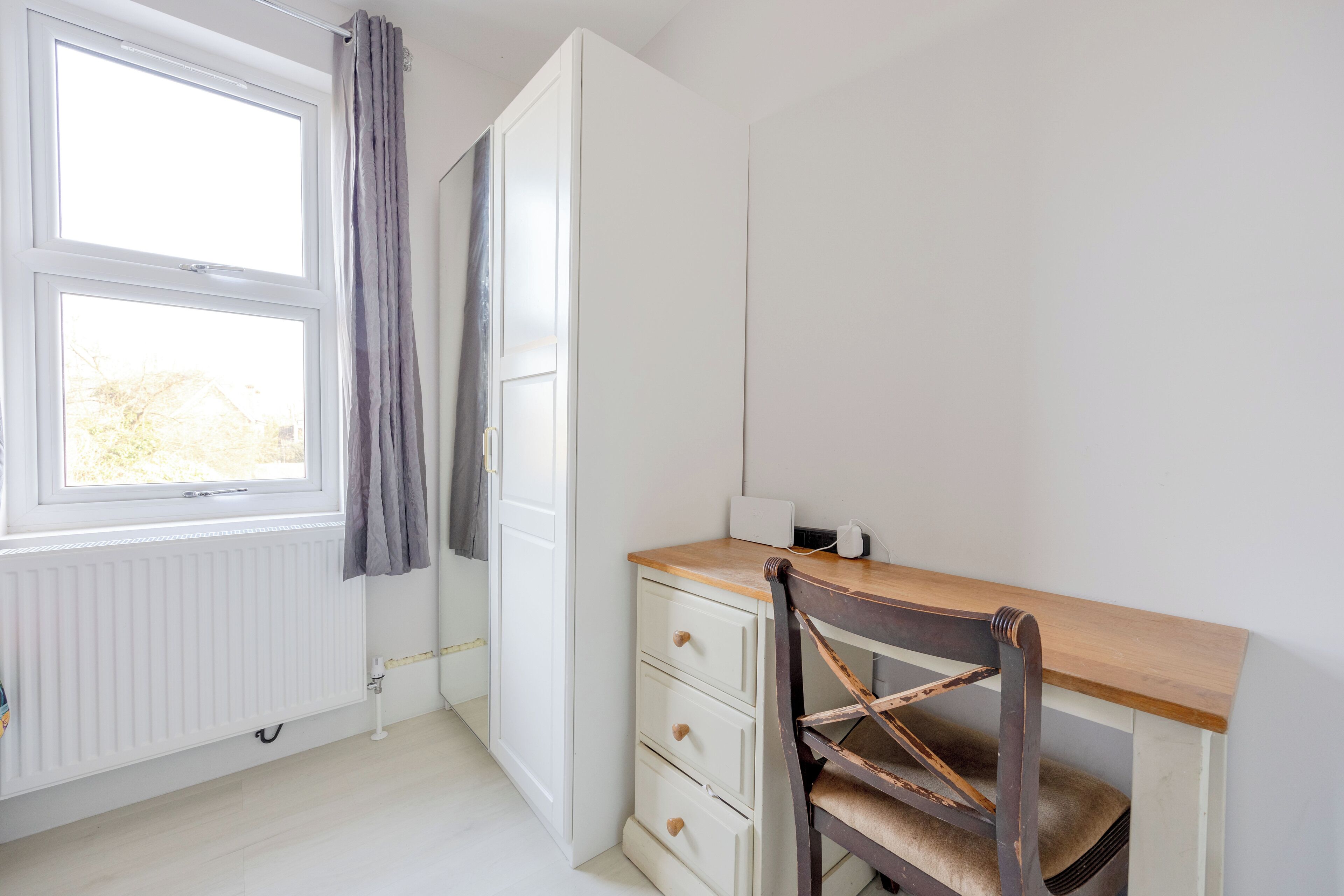 Een kamer met een houten bureau, een stoel, een radiator en een raam met gordijnen.