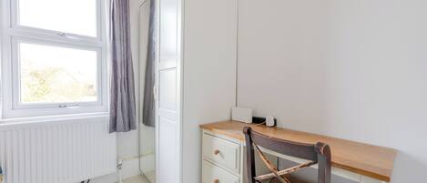 A room with a wooden desk, a chair, a radiator, and a window with curtains.