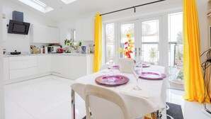 A modern kitchen with white cabinets, a built-in microwave, and a dining area with a table set for two. - Wavertree Hotel (London)