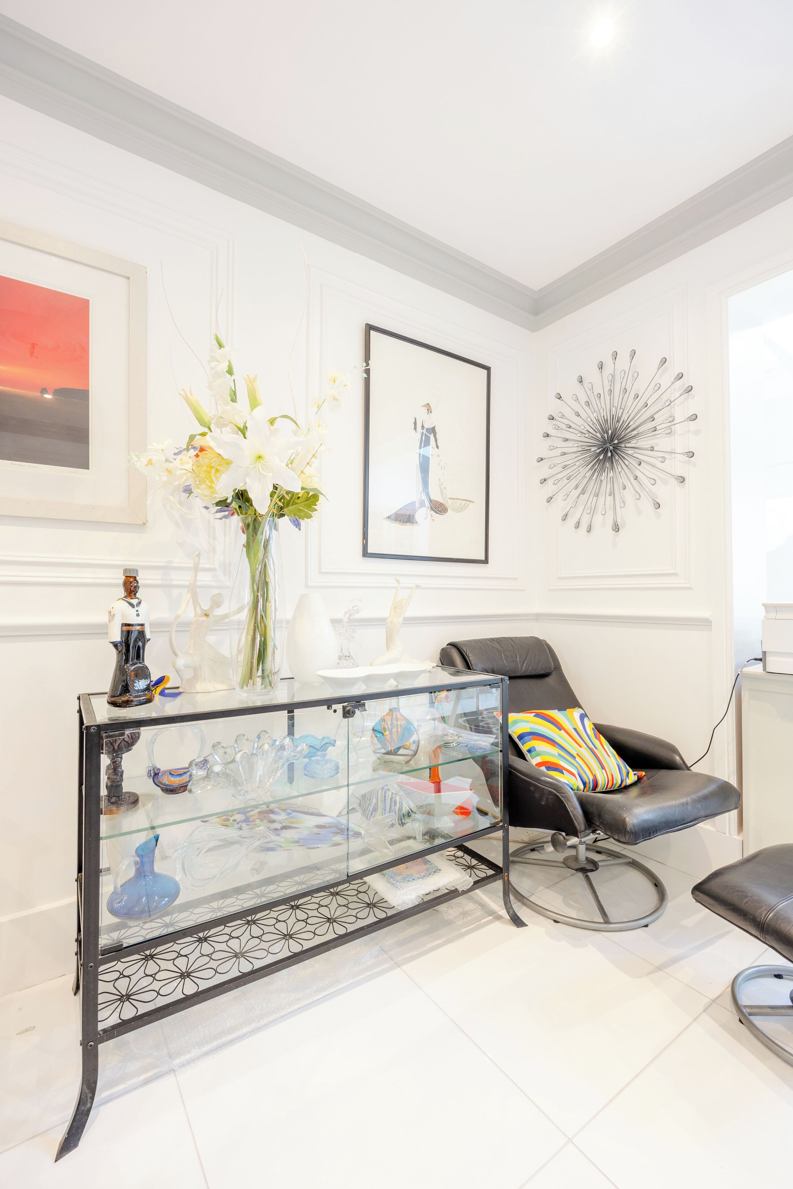 A modern living room with a glass coffee table, a black leather chair, and a colorful pillow.