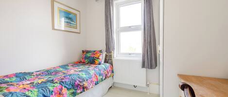 A bedroom with a bed, a window with curtains, a radiator, and a wooden dresser.