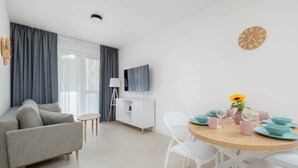 Un saló modern amb un sofà, una taula de dinar posta amb plats i gots, un televisor a la paret i un rellotge.