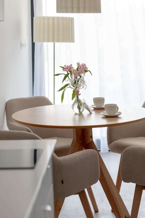 A round wooden table with a vase of pink flowers and two white cups.