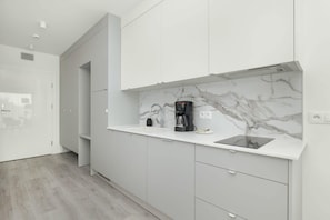 A modern kitchen with white cabinets, a marble backsplash, a coffee maker, and a built-in oven.