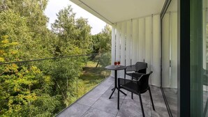 Ein Balkon mit Tisch und Stühlen, einer Glasumlaufung und Blick auf Bäume und Grün.