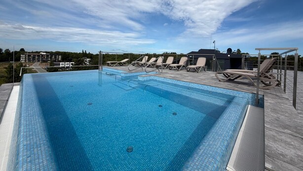 Ein rechteckiger Swimmingpool mit klarem, blauem Wasser, umgeben von Liegestühlen und einem überdachten Bereich mit Metallveranda.