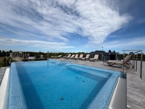 A rectangular swimming pool with clear blue water, surrounded by lounge chairs and a covered area with a metal roof. - Comfortable Studio in Mielno | Pool on the Roof and Parking (Mielno)