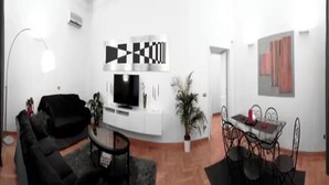 Ein modernes Wohnzimmer mit einer schwarzen Couch, einem Fernseher und einem Essbereich mit Tisch und Stühlen.