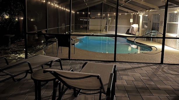 A covered outdoor swimming pool area with lounge chairs and a view of the pool through a glass enclosure. - Tranquil Pool Home Minutes to Siesta Key (Sarasota)
