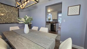 A dining area with a long table, white chairs, a vase with flowers, and a patterned rug. - Tranquil Pool Home Minutes to Siesta Key (Sarasota)