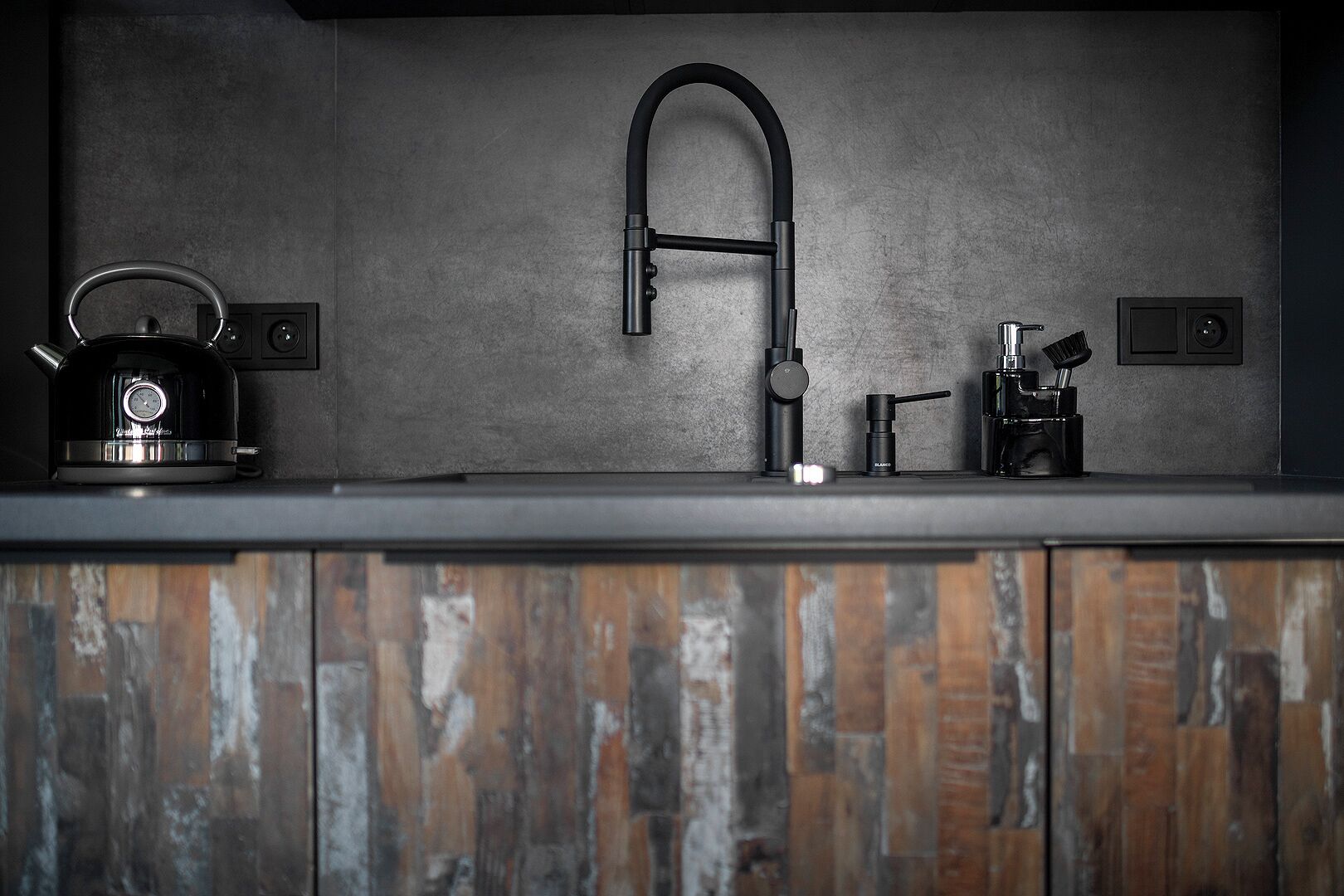 A kitchen with a modern faucet, a kettle, and a coffee machine on a wooden countertop.