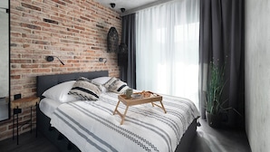 Une chambre moderne avec un mur en briques, un grand lit avec une literie à rayures, une table de chevet avec une lampe et une fenêtre avec des rideaux.