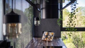 Un intérieur moderne avec une table en bois sur laquelle est posé un magazine, des lampes suspendues et une vue sur la verdure à l’extérieur.