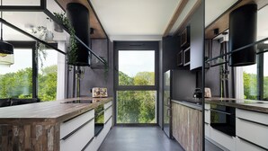 Une cuisine moderne dotée d’un îlot central, de grandes fenêtres et offrant une vue sur la verdure.