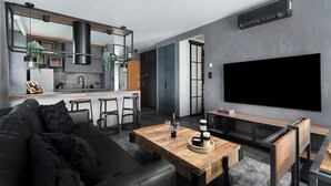 Un salon moderne avec un grand téléviseur à écran plat, une table basse en bois et un canapé en cuir noir.