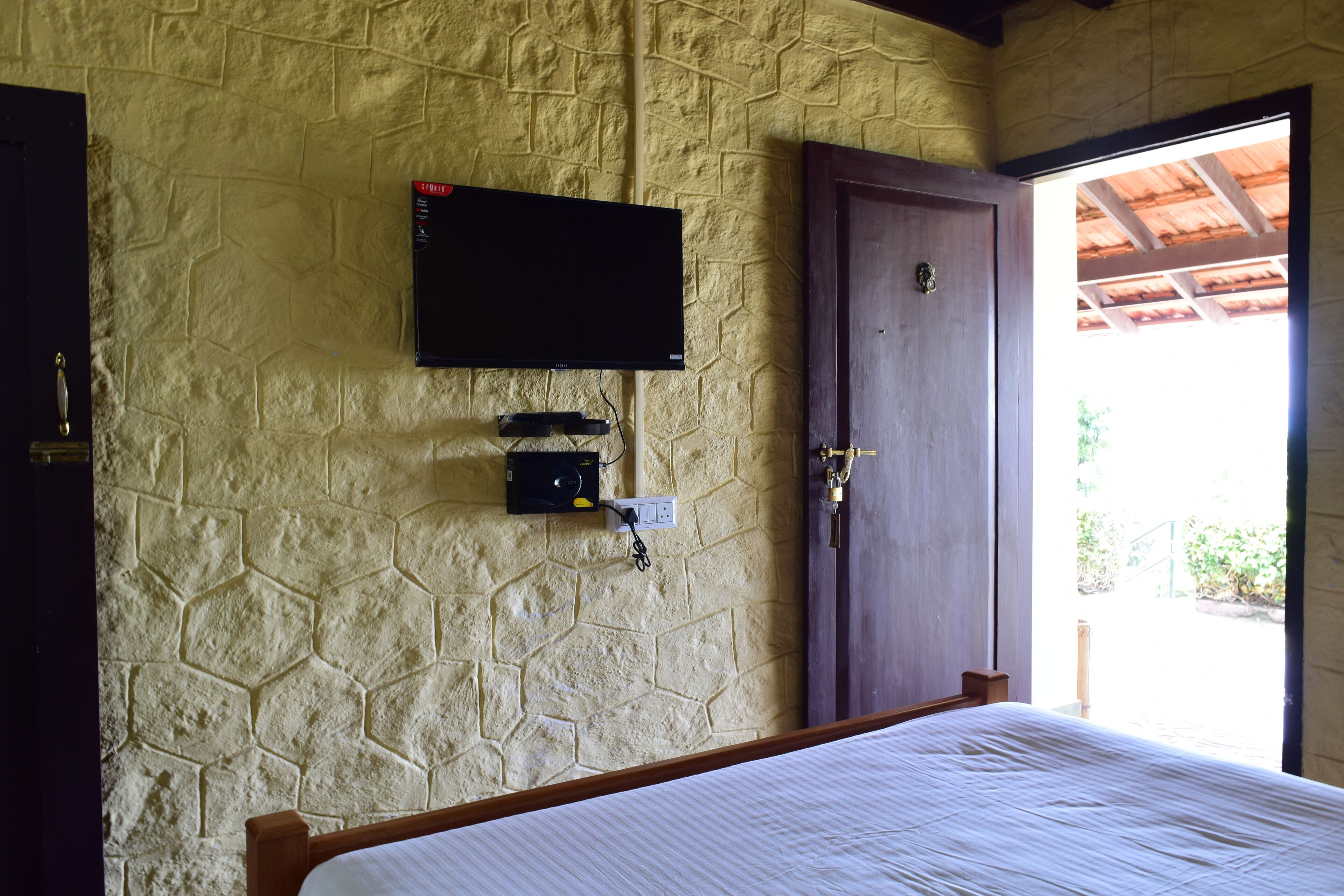 Un dormitorio con pared de piedra, televisor montado sobre un enchufe y una puerta de madera.