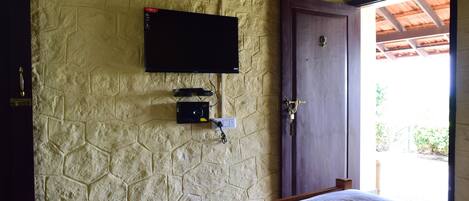 Un dormitorio con pared de piedra, televisor montado sobre un enchufe y una puerta de madera.