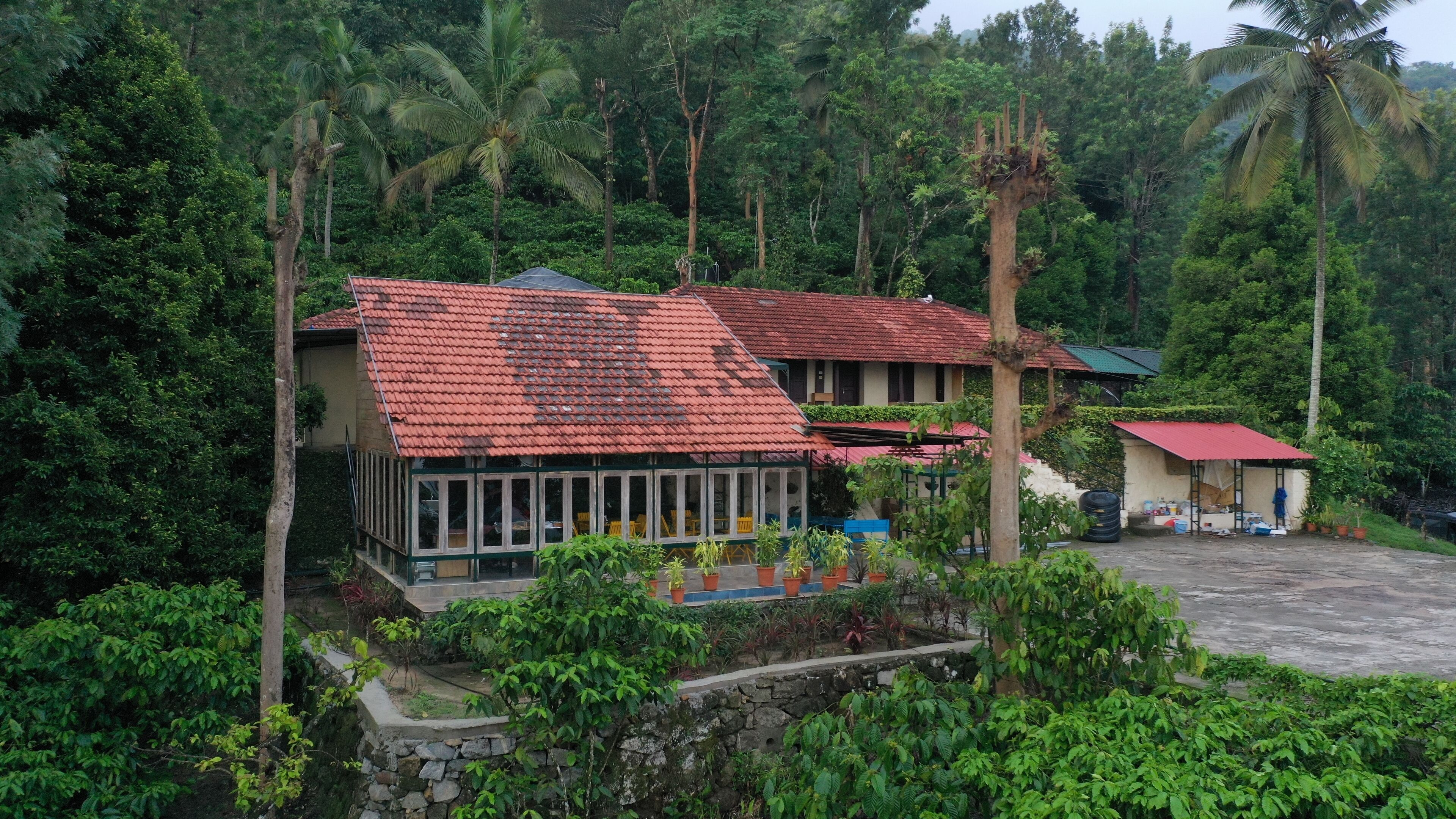 A two-story building with a red-tiled roof, surrounded by lush greenery and palm trees.