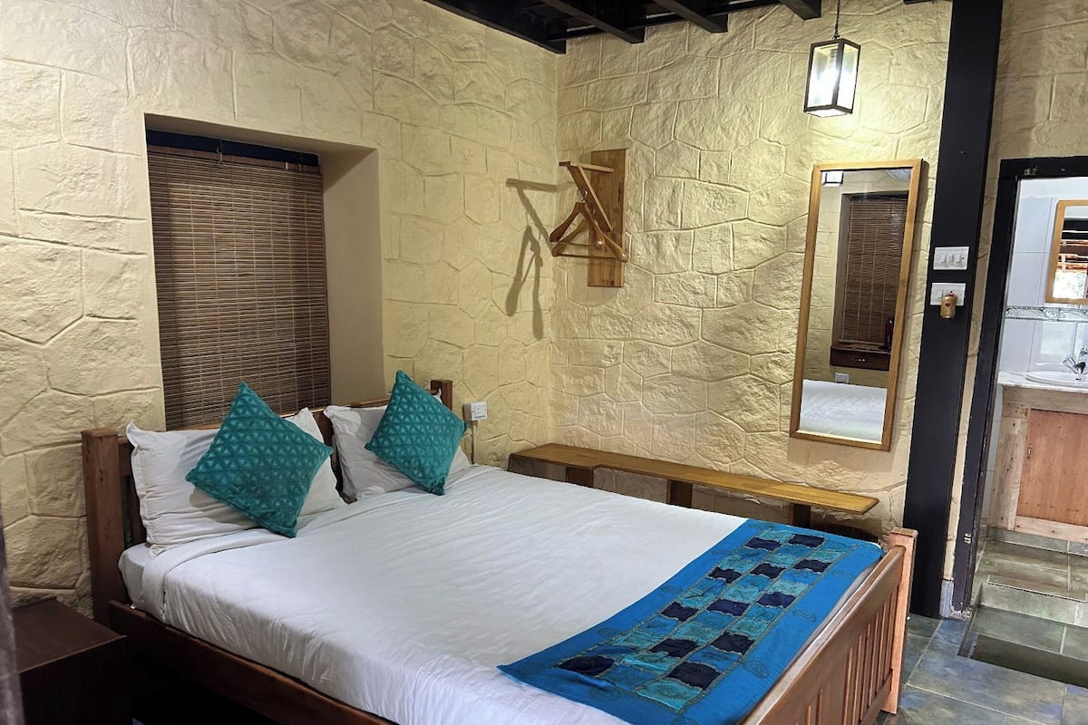 A bedroom with a stone wall, a wooden bed frame, a bedside table, and a mirror.