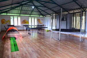 Un espacio interior amplio con techo alto, un trampolín, una mesa con sillas y una colchoneta verde para ejercicios.