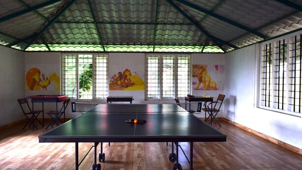 Une pièce spacieuse équipée d’une table de ping-pong, dotée d’un plancher en bois et de grandes fenêtres avec des barreaux en métal.
