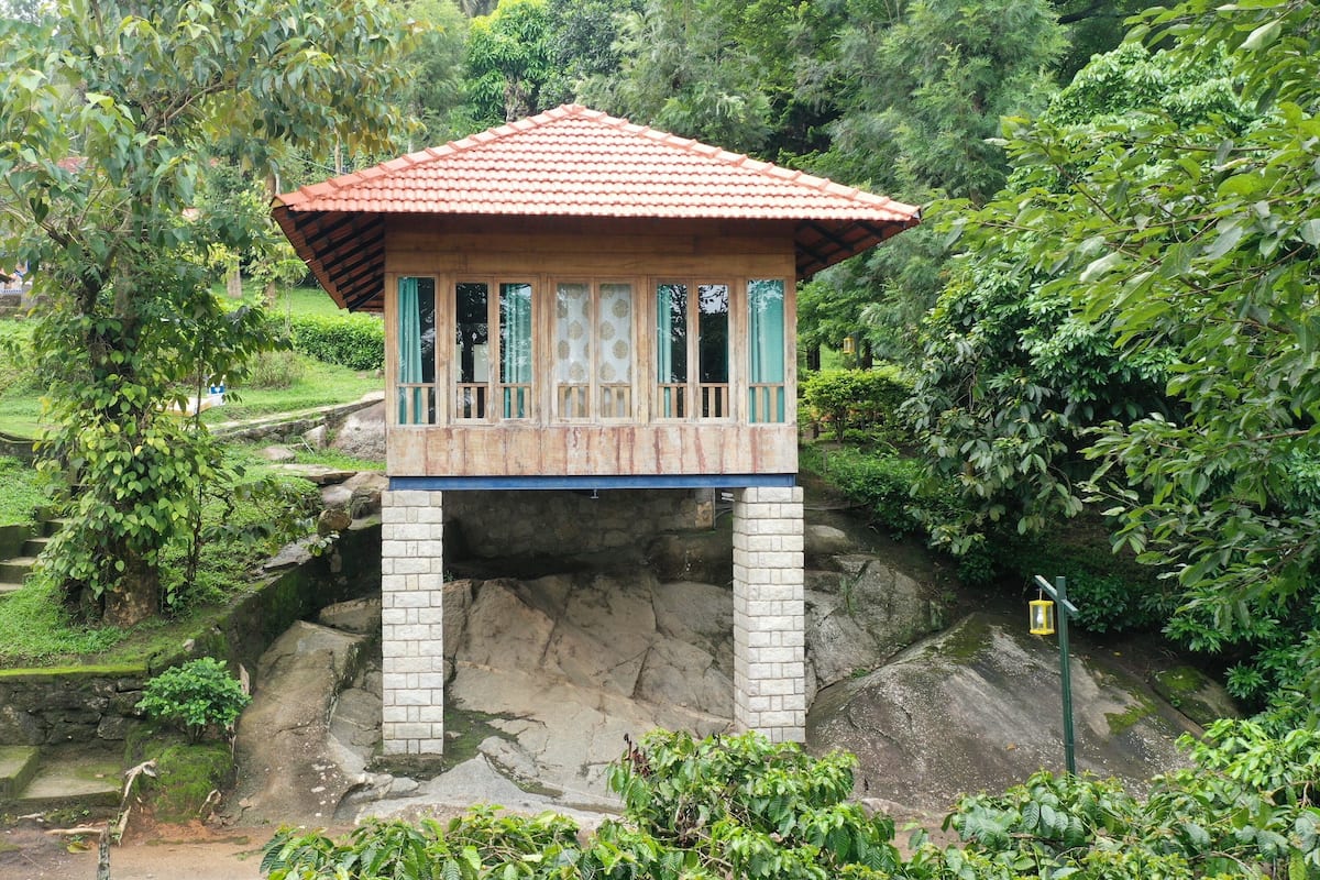 A wooden structure with a tiled roof, built on a stone base, surrounded by lush greenery and a stone staircase.