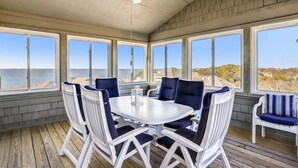 A sunroom with a large table and chairs, large windows, and a ceiling fan. - Waters, Ships Watch Community in Duck NC (Duck)