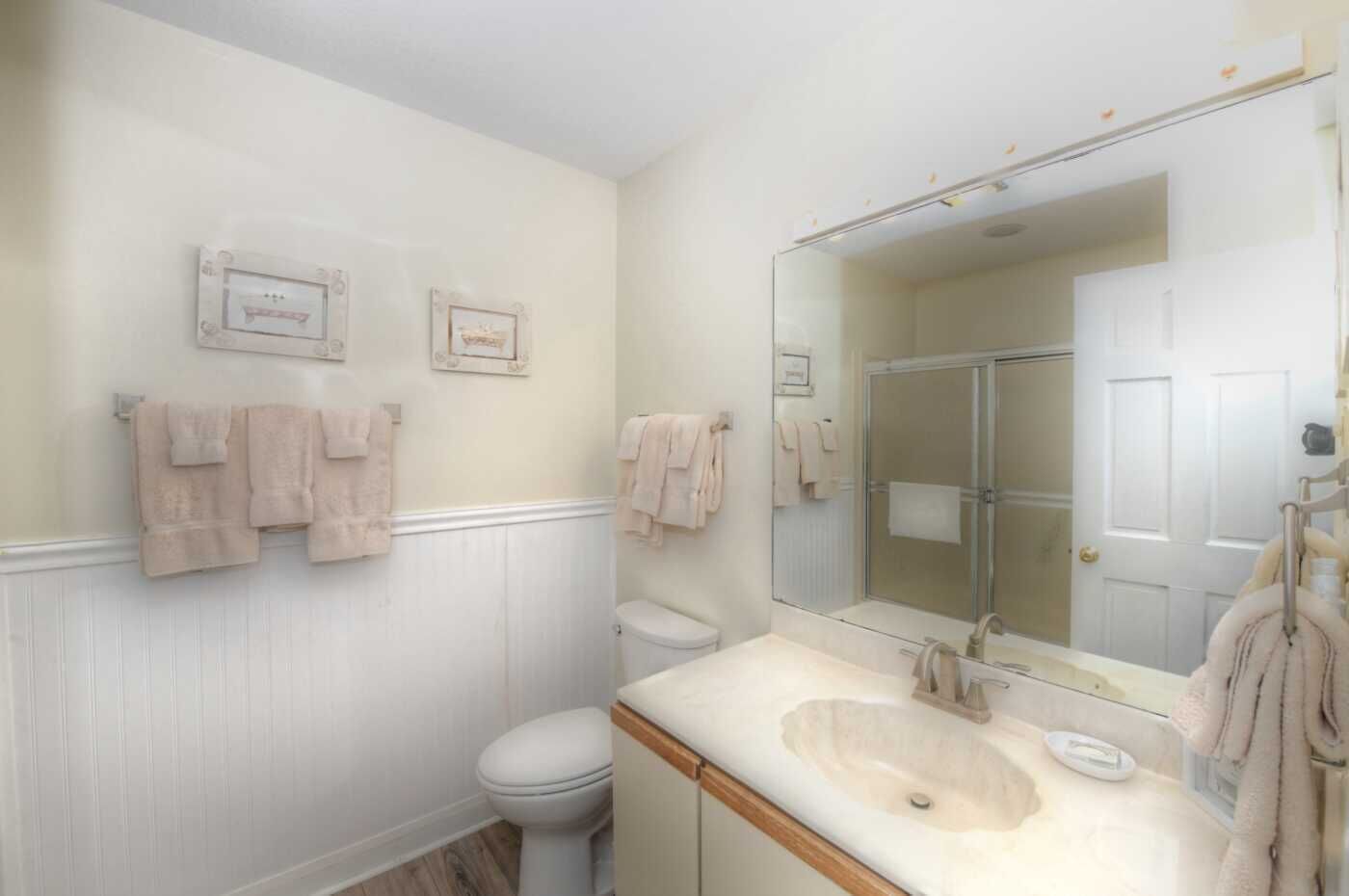 A bathroom with a white vanity, a large mirror, and two framed pictures on the wall.