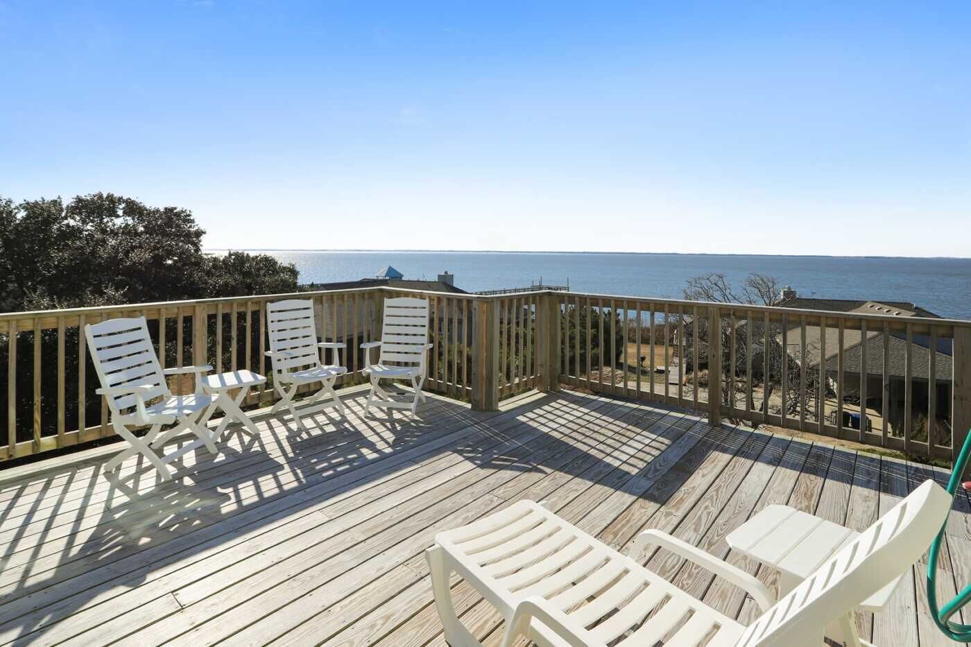 A wooden deck with white chairs and a table, overlooking a body of water.