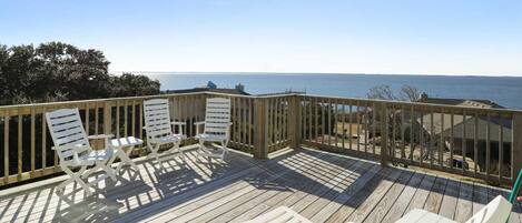 A wooden deck with white chairs and a table, overlooking a body of water.