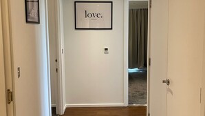 Un pasillo con suelo de madera, paredes blancas y un cartel enmarcado que dice "love". Hay puertas a ambos lados y una lámpara en el techo.