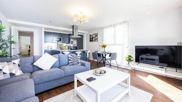 Una sala moderna con un sofá gris, una mesa de centro blanca y un televisor.