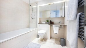 Un baño moderno con ducha vidriada, inodoro, lavamanos con espejo y un perchero para toallas.