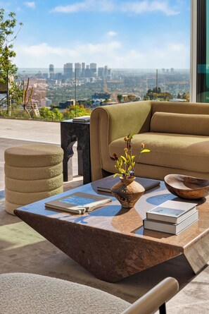 A modern living room with a sofa, ottoman, and coffee table, featuring a city view.