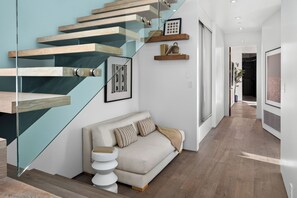 A modern interior with a staircase, a sofa, and a hallway leading to a door.