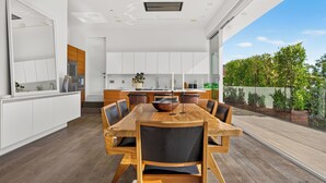 Una cocina moderna con armarios blancos, un comedor con mesa y sillas de madera, y vista a un jardín.