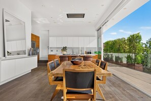 Una cucina moderna con mobili bianchi, un'area pranzo con tavolo e sedie in legno, e vista su un giardino.
