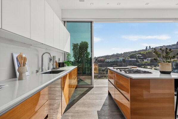 A modern kitchen with a large island, wooden cabinets, and a view of a cityscape.