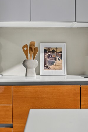 A kitchen counter with a white vase holding wooden kitchen utensils and a framed picture of a snowy street scene.
