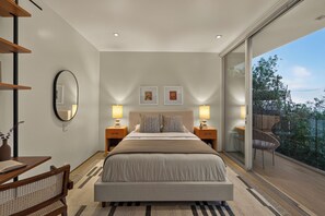 A bedroom with a large bed, two bedside tables with lamps, a mirror, and artwork on the wall.